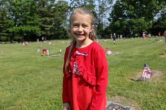 Young girl in red dress standing in front of graveyard.