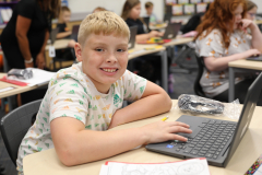 Young boy sitting at a desk in front of a laptop computer on the first day of school.