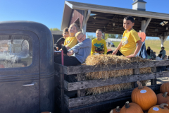 People sitting in a truck bed full of pumpkins at an apple orchard.