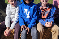 Three boys sitting on a hay bale at an apple orchard.