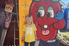 Little girl standing in front of apple orchard sign.