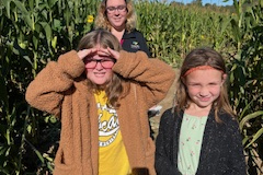 Three people standing in front of cornfield.