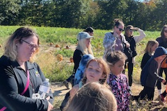 People standing in a field of pumpkins, possibly at an apple orchard.