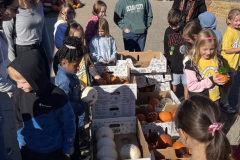 People gathered around a table filled with pumpkins at an apple orchard.