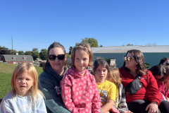 Family sitting on hay bale at apple orchard.