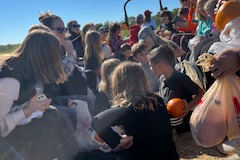 People sitting in a field, gathered around a truck, with some holding bags of groceries and others interacting with each