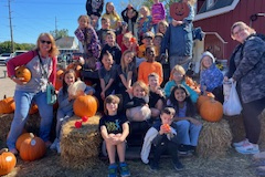 Group of people posing in front of a hay bale with pumpkins, smiling at the camera.