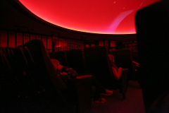 Empty movie theater seats in a dark room with a red light on the ceiling.