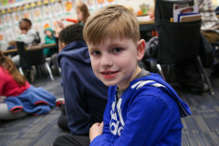 Boy in blue hoodie sitting on floor in classroom.