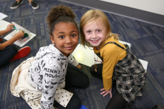 Two young girls posing for a picture in an indoor setting, one wearing a black and white plaid skirt and the other in a