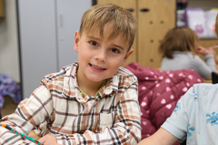 Two young boys sitting at a table in a classroom, smiling at the camera.