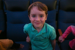 Boy in a theater seat, smiling at the camera.