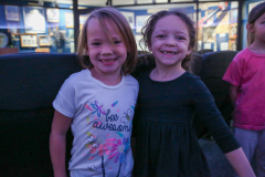 Two young girls posing together in front of a museum display.