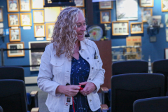 Woman in a blue shirt standing in front of a display case filled with plaques and trophies.