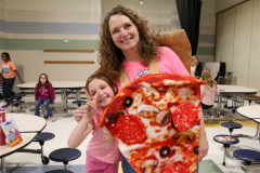 Woman in pink shirt holding child in front of pizza costume.