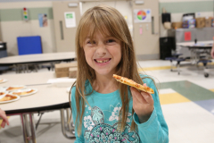 Girl holding slice of pizza in school cafeteria.