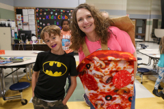 Woman in pink shirt holding pizza box, standing next to man in black t-shirt and jeans.