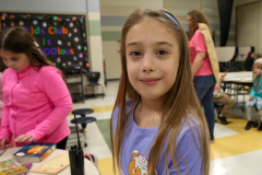 Young girl in a classroom setting, smiling at camera.