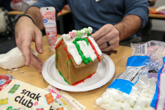 Man decorating gingerbread house with candy canes and other festive decorations.