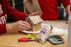 Person decorating gingerbread house with frosting and candy.