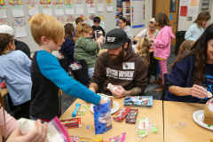 People gathered around a table with food and treats, engaging in conversation and enjoying themselves.