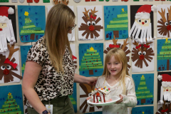 A woman in a black shirt is holding a plate of gingerbread cookies to a little girl.