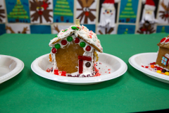 Three gingerbread houses on plates, decorated for Christmas, with candy canes and red velvet bow ties.