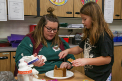Woman and child building gingerbread house in classroom.