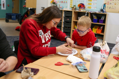 This is a photograph of a woman and a child in an indoor setting, possibly a classroom, where they are engaged in an