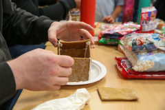 This is a photograph of a person in the process of making gingerbread houses. They are carefully placing pieces together on
