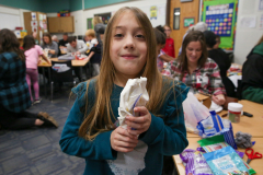 Young girl in classroom holding treat, smiling at camera.