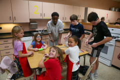 Children in a kitchen preparing food; adults supervising them.