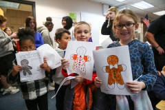 Children holding gingerbread people drawings in a classroom setting.