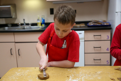 Boy in red apron decorating gingerbread cookies at kitchen counter.