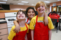 Three children in aprons posing for a picture in a kitchen.