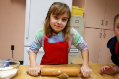 Little girl in kitchen, kneading dough at counter, smiling at camera.