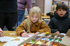 Two children sitting at a table filled with art supplies, engaged in an activity.