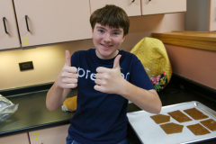 Boy giving thumbs up in kitchen, standing near cookie dough.