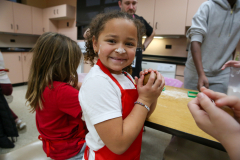 Girl in white shirt smiling at camera while sitting at table.