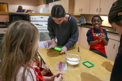 Woman in kitchen with children making gingerbread houses.