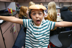Boy in striped shirt making a silly face while holding a gingerbread man on his head.