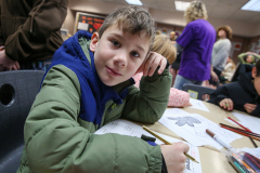 Young boy sitting at table drawing.