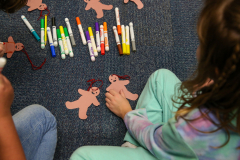 Children sitting on floor surrounded by colorful markers and crayons, creating art.