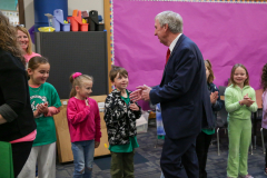 Man in suit standing among children clapping.