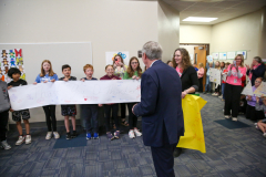 A man in suit stands among a group of children holding up signs, all smiling at the camera.