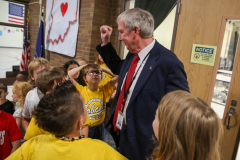 Man in suit standing among group of people, giving a thumbs up gesture.