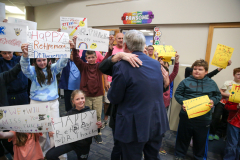People holding signs in front of a man at podium, celebrating an event.