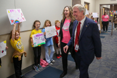Man in suit walking past children holding signs.