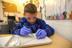 A young boy in a lab coat working on an owl pellet dissection at a desk.