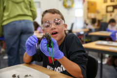 Boy in lab coat holding owl pellet, smiling at camera.